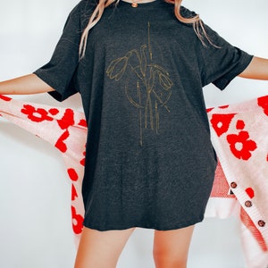 May include: A black oversized t-shirt with a gold floral design featuring stylized flowers and geometric lines.