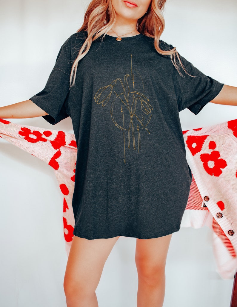 May include: A black oversized t-shirt with a gold floral design featuring stylized flowers and geometric lines.