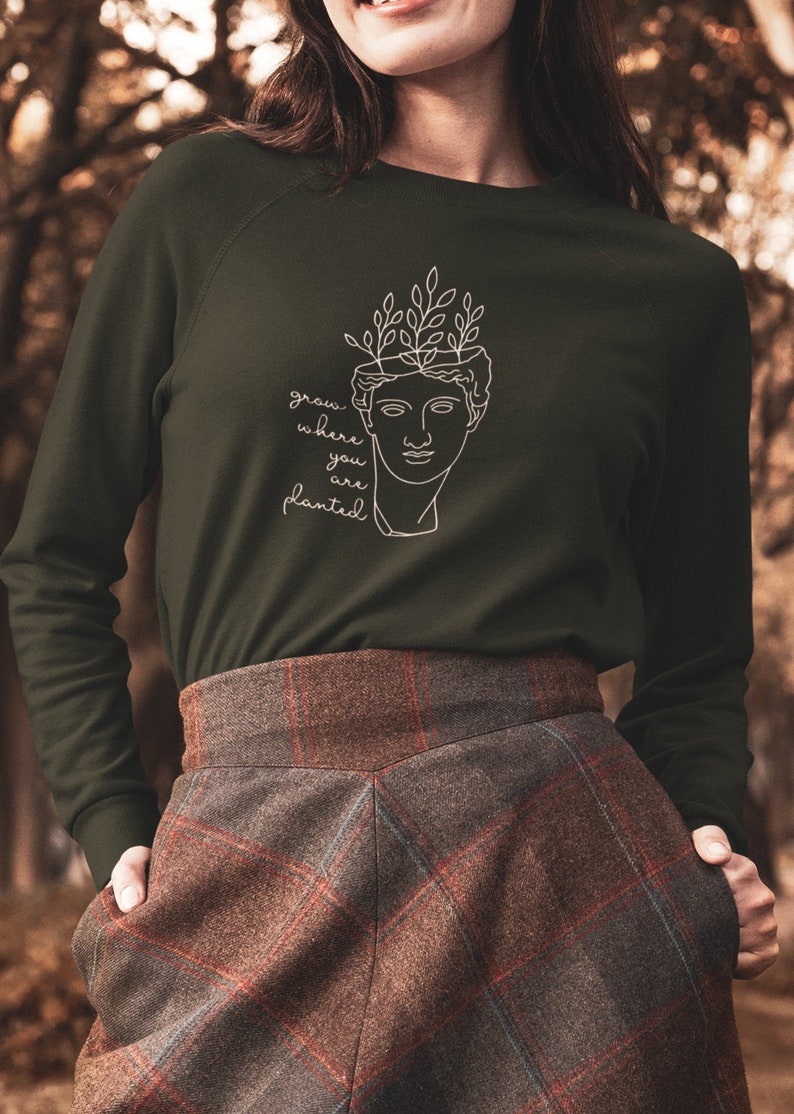 May include: A dark green sweatshirt with a white line drawing of a bust with leaves growing out of the top. The text "grow where you are planted" is written below the bust.