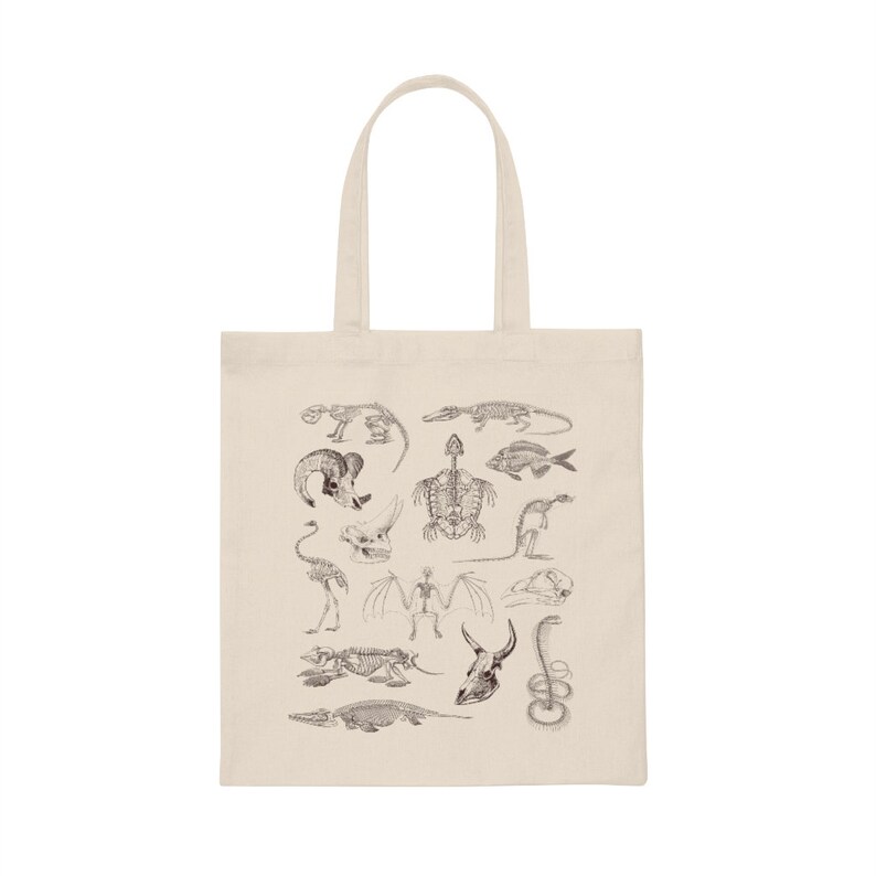 Peut inclure: Un sac fourre-tout beige avec un imprim&eacute; noir et blanc de divers squelettes d'animaux. Les squelettes comprennent un poisson, une tortue, un oiseau, une chauve-souris, un serpent, un crocodile, un dinosaure et un cr&acirc;ne.