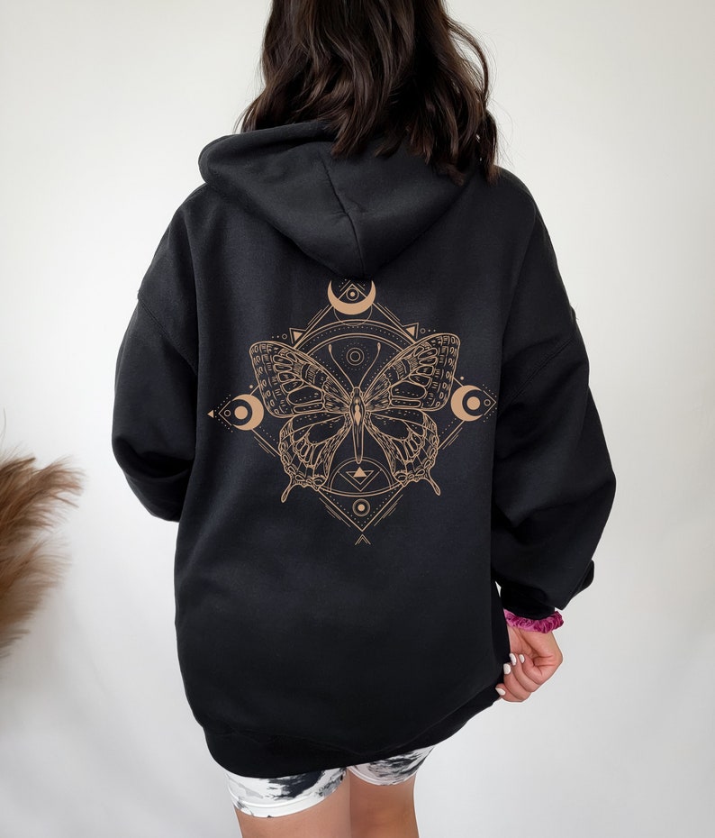May include: Black hooded sweatshirt with a gold butterfly graphic on the back. The butterfly is surrounded by geometric shapes and crescent moons.
