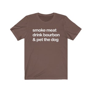 May include: A brown t-shirt with the text "smoke meat drink bourbon & pet the dog" printed in white.