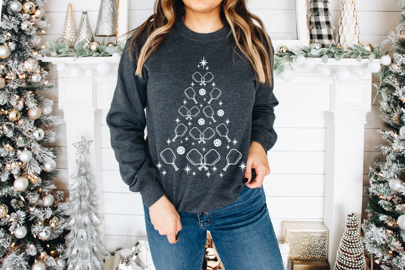 K&ouml;nnte beinhalten: Ein dunkelgraues Sweatshirt mit einem wei&szlig;en Design eines Weihnachtsbaums aus Pickleball-Schl&auml;gern und B&auml;llen.