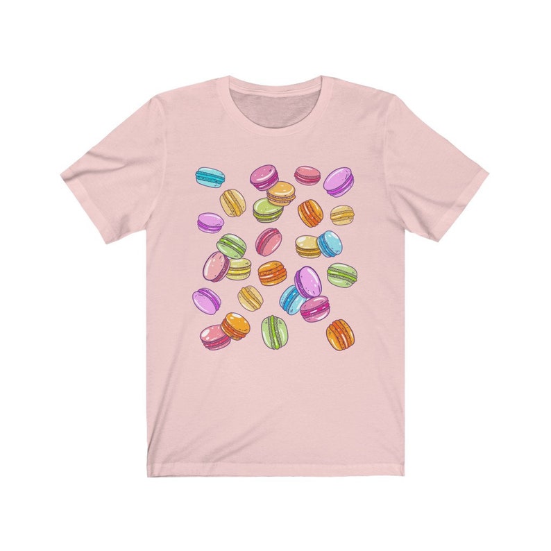 May include: A pink t-shirt with a colorful macaron pattern. The macarons are in various shades of pink, blue, green, yellow, and orange.