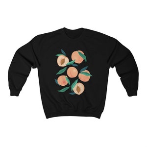 K&ouml;nnte beinhalten: Schwarzer Pullover mit einem Grafikdruck von Pfirsichen mit gr&uuml;nen Bl&auml;ttern.
