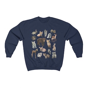 May include: A navy blue sweatshirt featuring a pattern of various woodland animals, including a bear, deer, fox, rabbit, raccoon, and owl. The animals are all depicted in a cartoon style and are arranged in a random pattern.