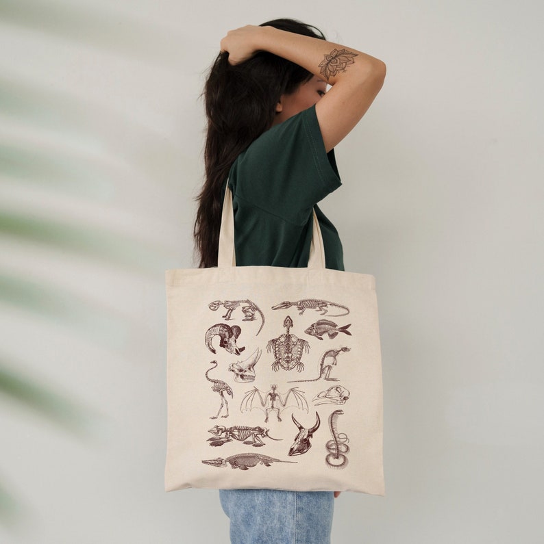 Peut inclure: Un sac fourre-tout beige avec un motif de squelettes d'animaux vari&eacute;s en brun. Les squelettes comprennent une tortue, un poisson, un oiseau, et plus encore.