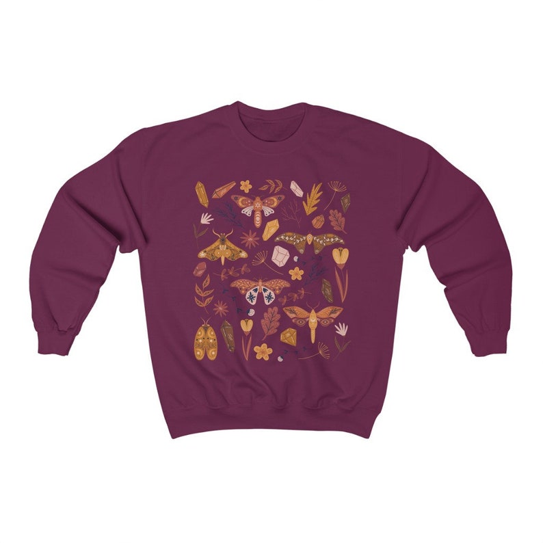 Puede incluir: Una sudadera color granate con un patr&oacute;n colorido de polillas, cristales y hojas. El dise&ntilde;o presenta una variedad de especies de polillas, incluyendo polillas luna, polillas halc&oacute;n y polillas esfinge.