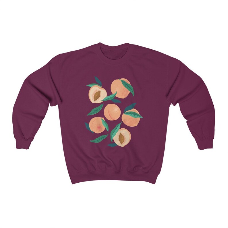 K&ouml;nnte beinhalten: Ein maroonfarbener Pullover mit einem Grafikdruck von Pfirsichen mit gr&uuml;nen Bl&auml;ttern. Die Pfirsiche sind in einem Kreis angeordnet.