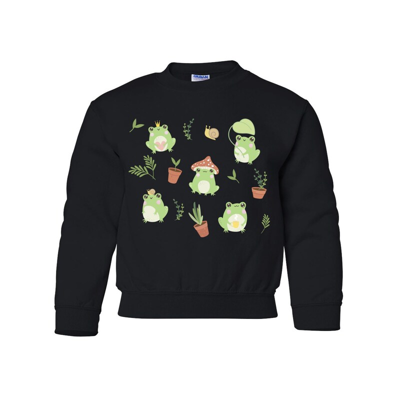 K&ouml;nnte beinhalten: Schwarzer Pullover mit einem Muster aus gr&uuml;nen Fr&ouml;schen und Pilzen. Die Fr&ouml;sche tragen Kronen und halten Blumen. Der Pullover hat einen Rundhalsausschnitt und lange &Auml;rmel.