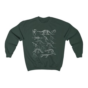 May include: A dark green sweatshirt with a white print of dinosaur skeletons. The print features a variety of dinosaurs, including a Stegosaurus, Triceratops, and Brachiosaurus.
