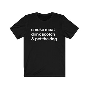 May include: Black t-shirt with white text that reads "smoke meat drink scotch & pet the dog"