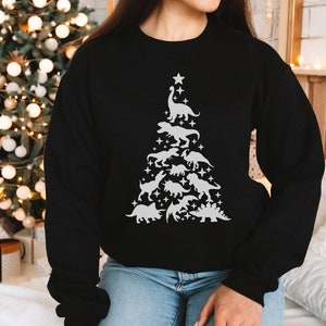 May include: Black sweatshirt with a white design of a Christmas tree made of dinosaurs. The tree is topped with a star and has a variety of dinosaurs, including a T-Rex, Triceratops, and Stegosaurus.