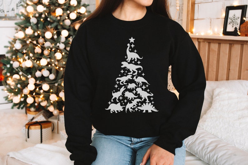 May include: Black sweatshirt with a white design of a Christmas tree made of dinosaurs. The tree is topped with a star and has a variety of dinosaurs, including a T-Rex, Triceratops, and Stegosaurus.