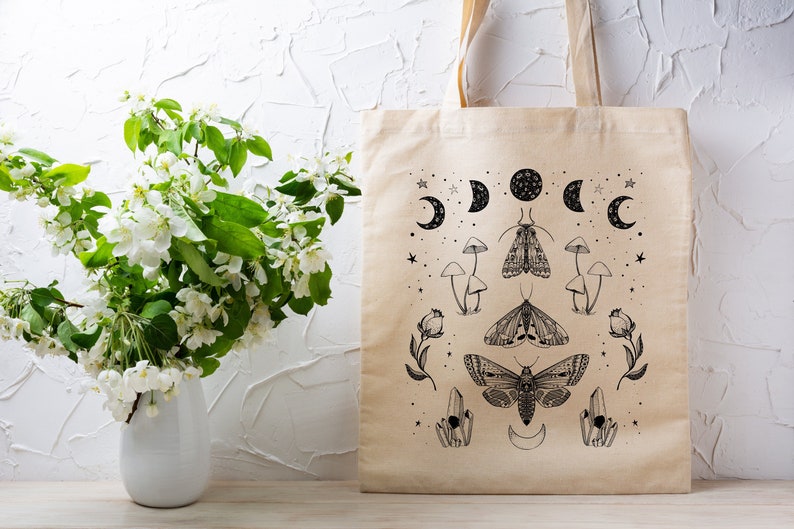 May include: A beige tote bag with a black and white design featuring moths, mushrooms, moons, and stars.
