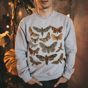 K&ouml;nnte beinhalten: Ein graues Sweatshirt mit einer Vintage-Illustration verschiedener Schmetterlinge und Motten in Braun-, Gelb- und Gr&uuml;nt&ouml;nen.