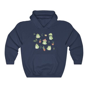 May include: A navy blue hoodie with a pattern of green frogs wearing different hats and accessories. The frogs are surrounded by small plants and flowers.