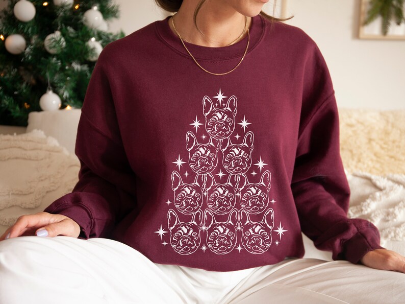 May include: A maroon sweatshirt with a white design of a Christmas tree made of French bulldog faces. The tree is decorated with white stars.