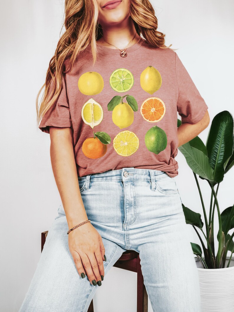Pode incluir: Uma camiseta malva com uma estampa gr&aacute;fica de nove frutas c&iacute;tricas, incluindo lim&otilde;es, limas, laranjas e toranjas. As frutas est&atilde;o dispostas em uma grade.