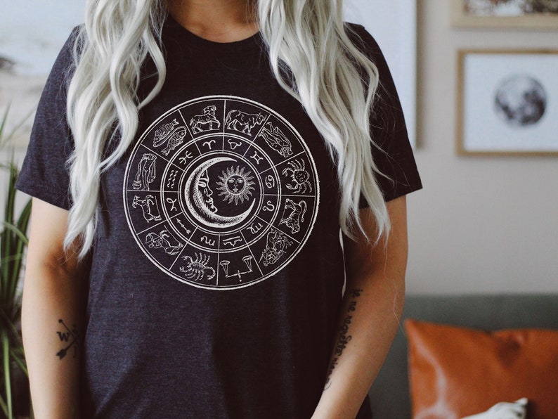 May include: A black t-shirt with a white graphic of a zodiac wheel featuring the twelve astrological signs and the sun and moon.