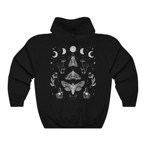 Pu&ograve; includere: Felpa con cappuccio nera con una stampa grafica bianca di falene, funghi e lune crescenti.