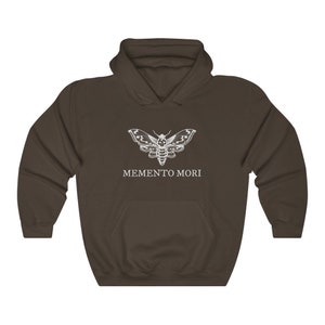 K&ouml;nnte beinhalten: Ein dunkelbraunes Kapuzenpullover mit einem wei&szlig;en Motiv eines Motten mit einem Totenkopf auf dem Kopf und dem Text "MEMENTO MORI" darunter.