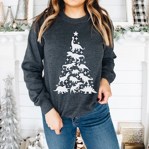 May include: A dark gray sweatshirt with a white silhouette of a Christmas tree made of dinosaurs. The tree is topped with a star.