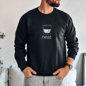 Pode incluir: Camisola de moletom preta com um gr&aacute;fico branco de um copo de licor e a palavra "neat" embaixo.