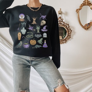 May include: A black sweatshirt with a Halloween-themed graphic print featuring various spooky icons like a skull, a cauldron, a ghost, a bat, a snake, a pumpkin, a witch's hat, and a raven.