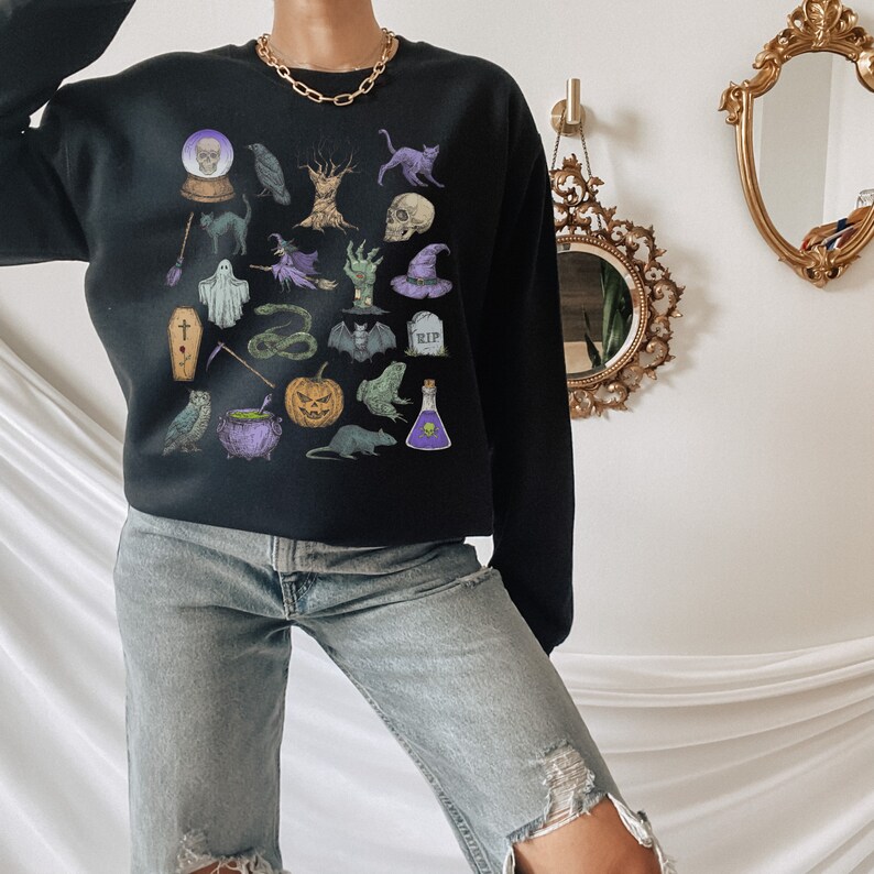 May include: A black sweatshirt with a Halloween-themed graphic print featuring various spooky icons like a skull, a cauldron, a ghost, a bat, a snake, a pumpkin, a witch's hat, and a raven.