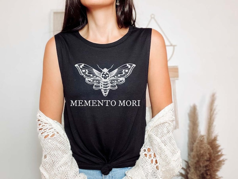 May include: Black sleeveless muscle tank top with a white graphic of a moth with a skull design and the text "MEMENTO MORI" printed below the moth.