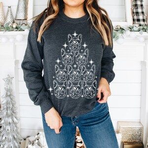 May include: A dark gray sweatshirt with a white outline of a Christmas tree made of French bulldog faces. The tree is decorated with stars.