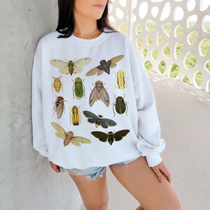 May include: White sweatshirt with a graphic print of various insects, including beetles, butterflies, and moths. The insects are depicted in a vintage style with detailed illustrations.