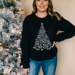 May include: A black sweatshirt featuring a white design of a Christmas tree made up of cat faces. The tree is decorated with stars.