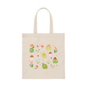 May include: A beige tote bag with a design of green frogs, flowers, mushrooms, and bees. The frogs are wearing flowers and hats.