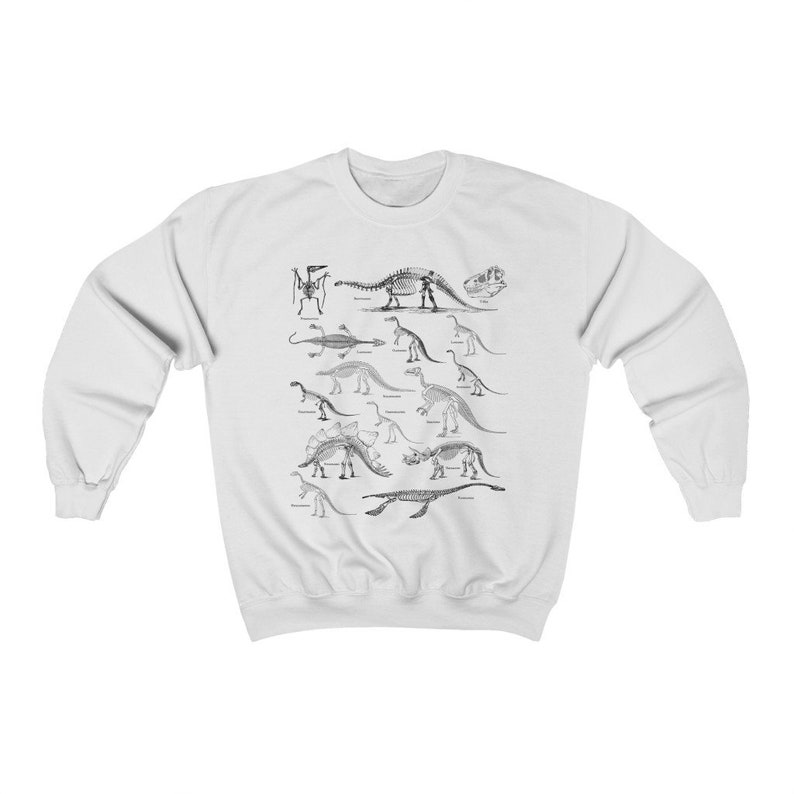 May include: White sweatshirt with a black and white illustration of dinosaur skeletons. The skeletons are arranged in rows and include a variety of dinosaurs, such as Stegosaurus, Triceratops, and Brachiosaurus.