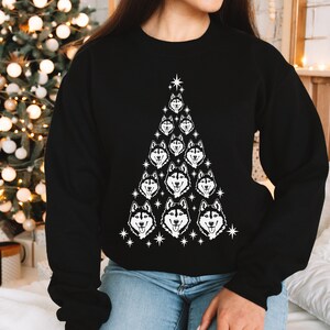 Puede incluir: Sudadera negra con un dise&ntilde;o de &aacute;rbol de Navidad blanco con m&uacute;ltiples caras de perros husky. El &aacute;rbol est&aacute; decorado con estrellas blancas.