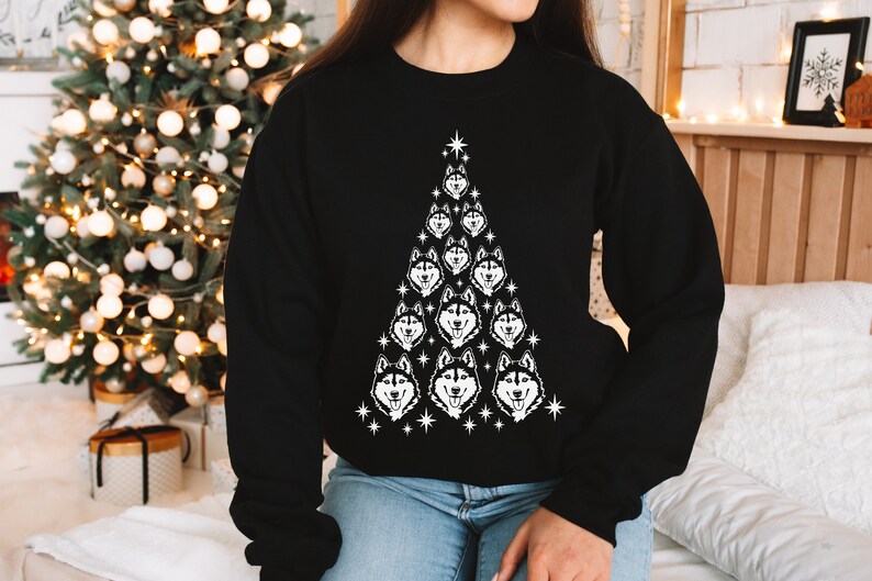 Puede incluir: Sudadera negra con un dise&ntilde;o de &aacute;rbol de Navidad blanco con m&uacute;ltiples caras de perros husky. El &aacute;rbol est&aacute; decorado con estrellas blancas.