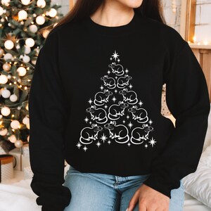 May include: A black sweatshirt with a white design of a Christmas tree made of rats. The tree is decorated with stars.