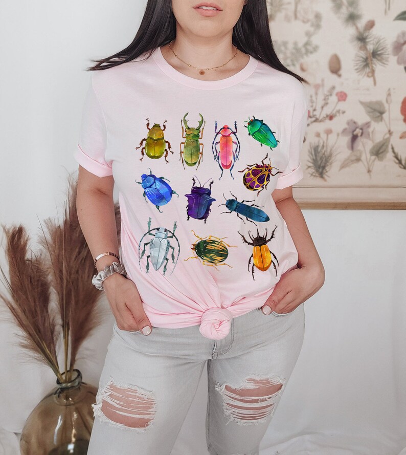 May include: A pink t-shirt with a colorful beetle design. The beetles are in various shades of green, blue, red, yellow, and purple.