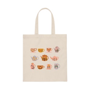 May include: A white canvas tote bag with a floral pattern of teacups and teapots in shades of pink, yellow, blue, and brown.