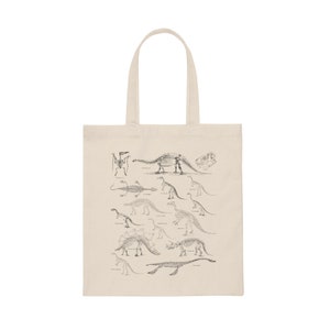 May include: A beige tote bag with a black and white illustration of dinosaur skeletons. The illustration includes a variety of dinosaurs, including a Stegosaurus, a Triceratops, and a Brachiosaurus.