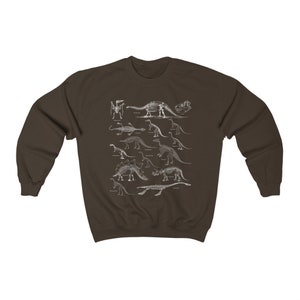 May include: A brown sweatshirt with a white print of dinosaur skeletons. The print features a variety of dinosaurs, including a stegosaurus, a triceratops, and a brachiosaurus.