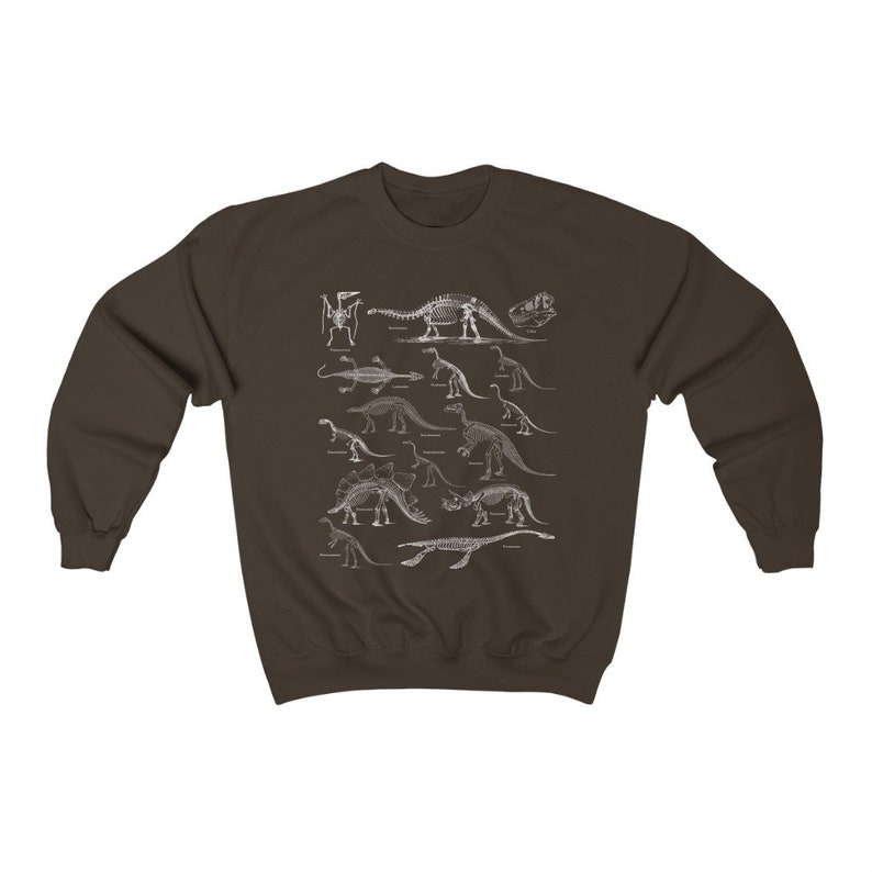 May include: A brown sweatshirt with a white print of dinosaur skeletons. The print features a variety of dinosaurs, including a stegosaurus, a triceratops, and a brachiosaurus.