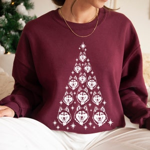 Puede incluir: Una sudadera color burdeos con un dise&ntilde;o de &aacute;rbol de Navidad blanco con m&uacute;ltiples caras de perros husky. El &aacute;rbol est&aacute; decorado con estrellas blancas.