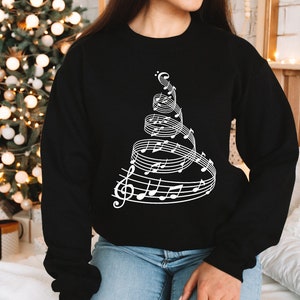 May include: Black sweatshirt with a white design of a Christmas tree made of musical notes.