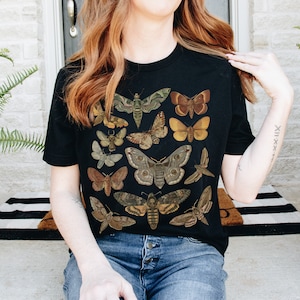 May include: Black t-shirt with a vintage illustration of various moths and butterflies in shades of brown, green, and yellow.