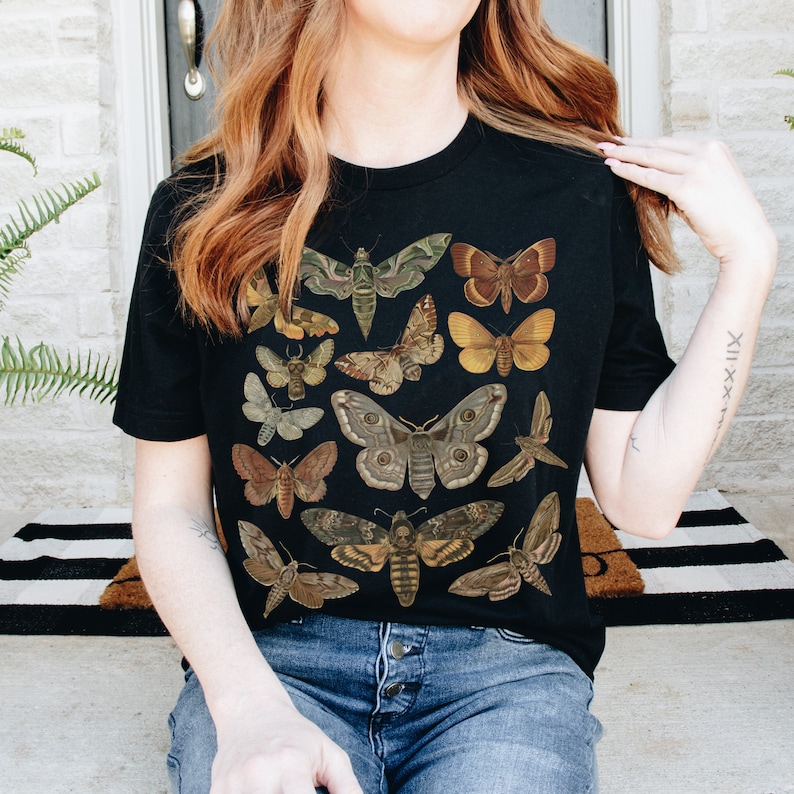 May include: Black t-shirt with a vintage illustration of various moths and butterflies in shades of brown, green, and yellow.