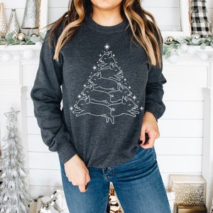 May include: A dark grey sweatshirt featuring a white outline of a Christmas tree made of pigs. The tree is topped with a star.
