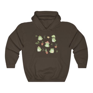 May include: A brown hoodie with a pattern of green frogs wearing crowns, hats, and sitting on mushrooms. The frogs are surrounded by green leaves and flowers.